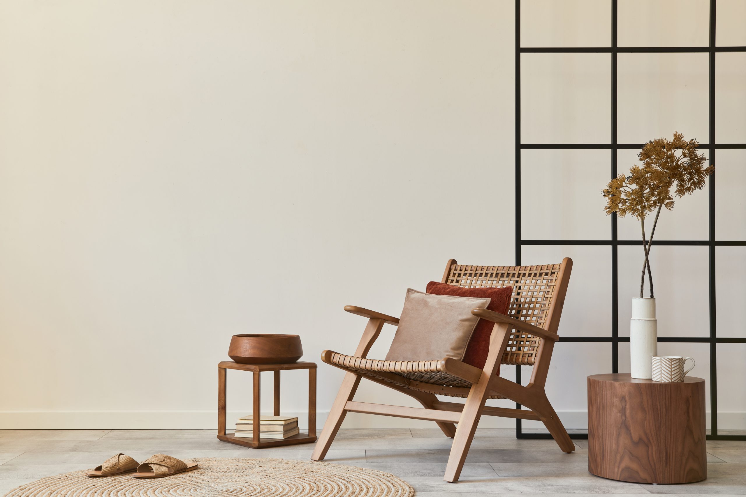 Stylish interior design of living room with wooden armchair, coffee table, furniture, rattan decoration, dried flowers and elegant personal accessories. Copy space white wall. Template.